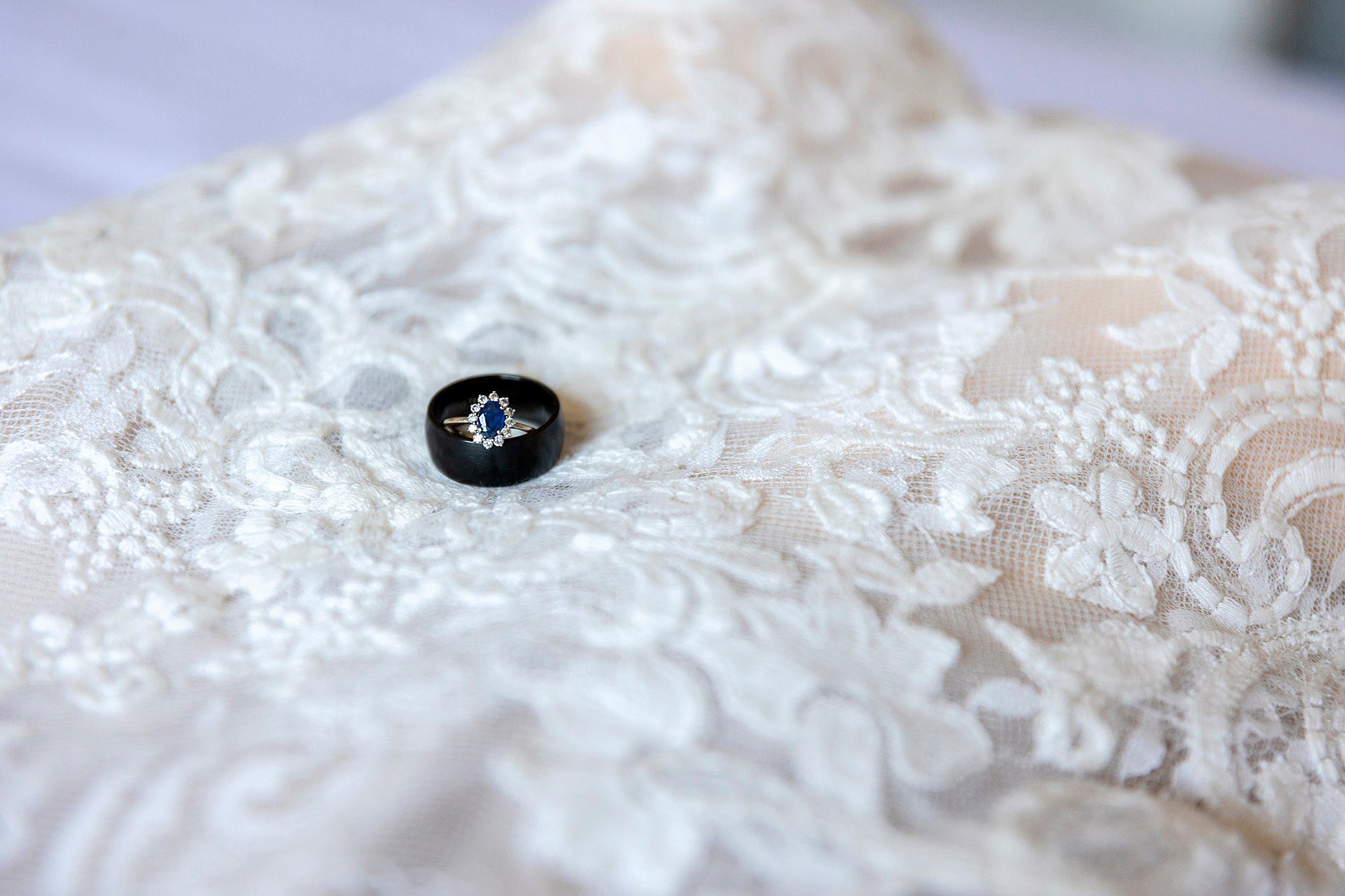 black wedding band and blue engagement ring sit on a white veil