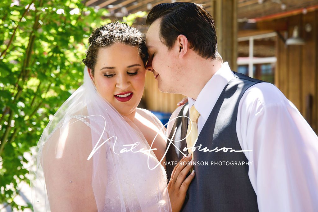 Groom nuzzles onto his new wife on a porch wearing a grey vest and yellow tie red barn farm wedding venue