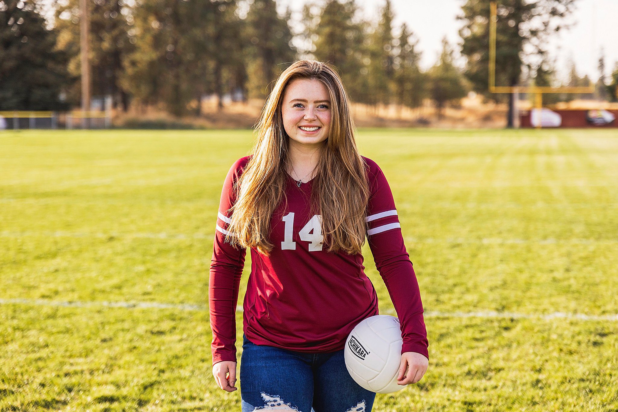 A high school senior stands on a football field wearing a volleyball jersey while holding a volleyball spokane tutors