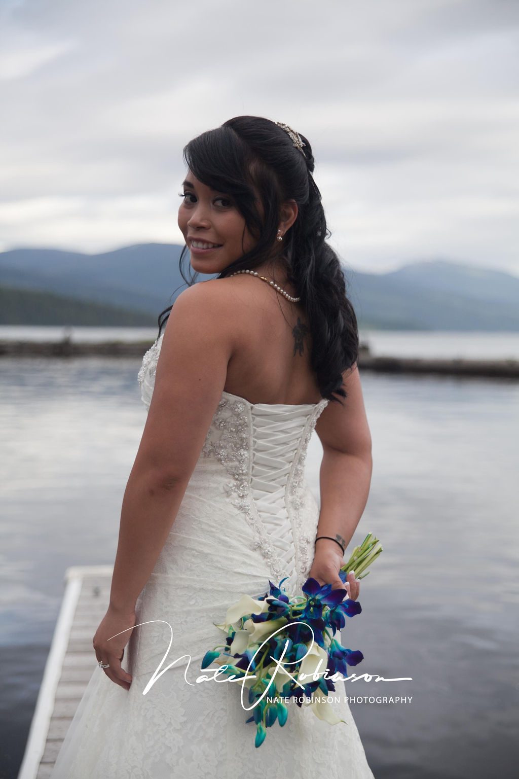 Bride in a white lace dress stands on a dock holding her blue bouquet zephyr lodge wedding