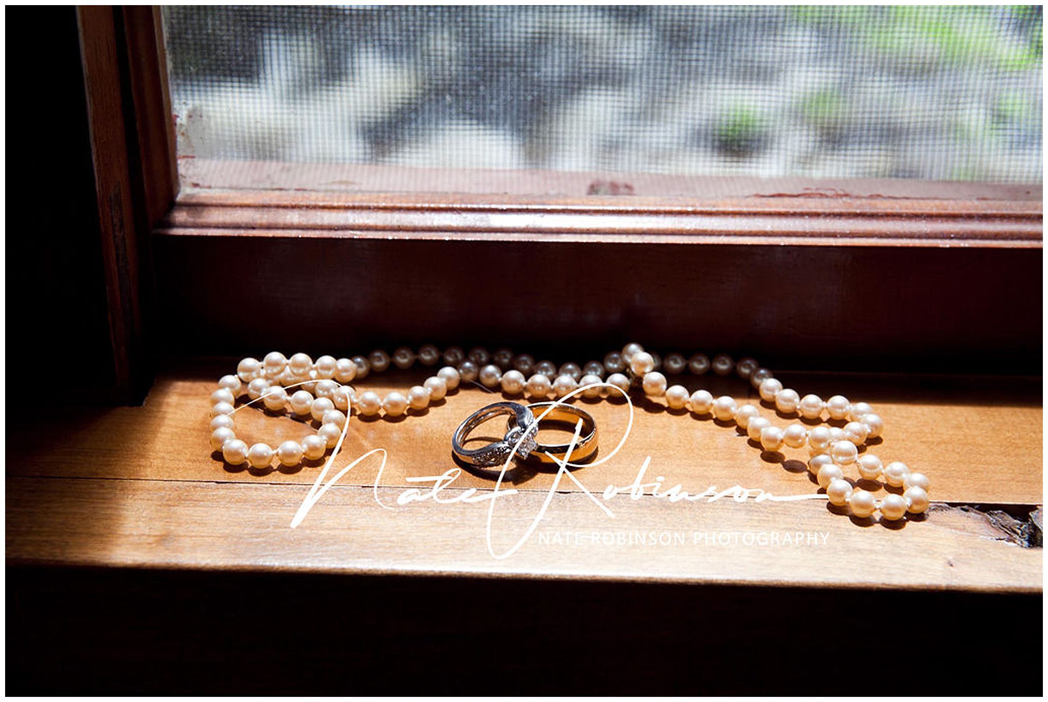A pearl necklace and wedding bands sit on a natural wooden window sill barrister winery wedding