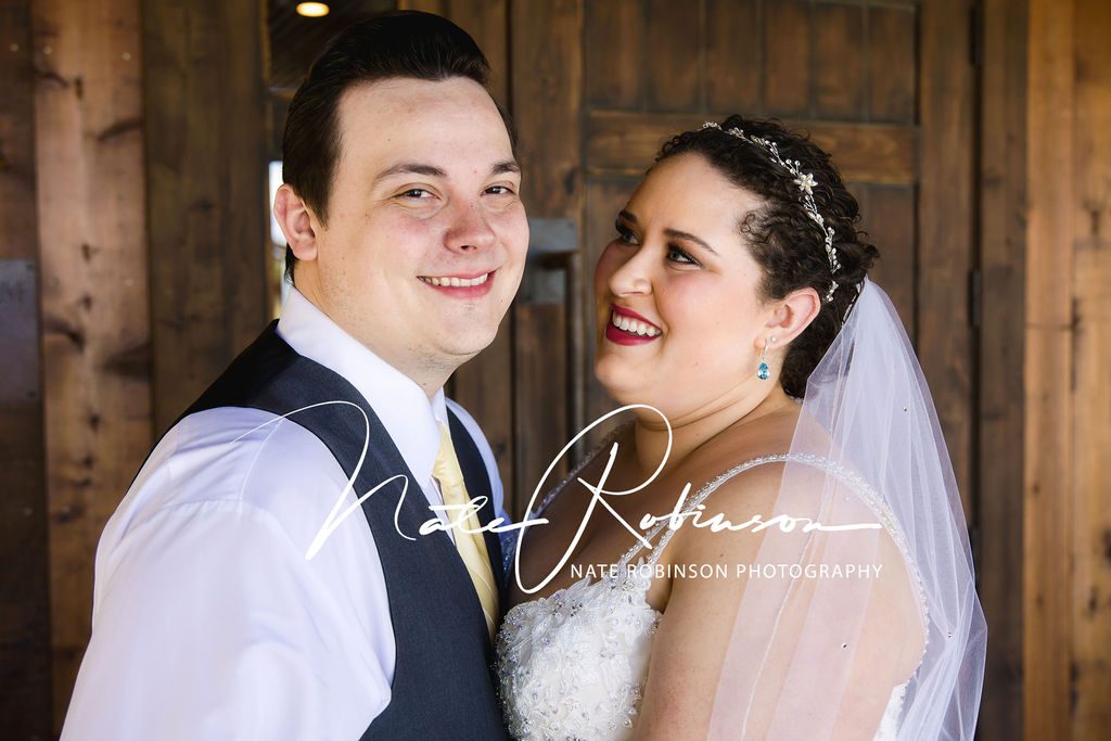 A newlywed could stand chest to chest in front of a rustic wooden door and wall at a rustic river wedding venue